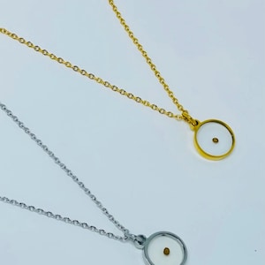 K&ouml;nnte beinhalten: Zwei Halsketten mit einem kleinen runden Anh&auml;nger. Eine Halskette hat eine goldene Kette und einen goldenen Anh&auml;nger. Die andere Halskette hat eine silberne Kette und einen silbernen Anh&auml;nger. Jeder Anh&auml;nger hat einen kleinen wei&szlig;en Kreis mit einem winzigen goldenen Punkt in der Mitte.