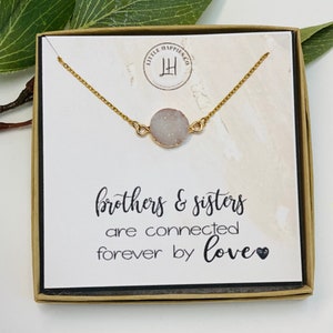 May include: A gold necklace with a white agate stone pendant in a box with the text "brothers & sisters are connected forever by love".