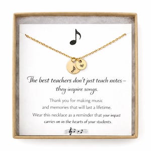 May include: Gold-colored necklace with two small round pendants, one with a musical note and the other with a heart. The necklace is presented in a gift box with text that reads, "The best teachers don't just teach notes - they inspire songs."