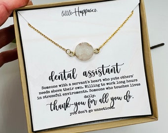 Op de afbeelding: Een klein cadeaudoosje met een gouden ketting en een witte kristallen hanger. Het doosje heeft een witte kaart met de tekst "tandartsassistente" en een bedankbericht.