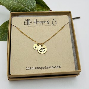 May include: Gold necklace with two charms, one with a heart and the other with a boxing glove. The necklace is in a brown box with the text "Little Happies Co. It is more blessed to give than to receive" and "littlehappiesco.com".