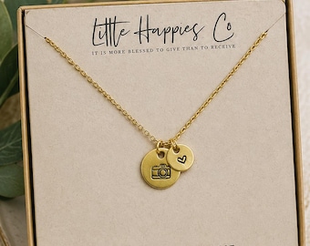 Puede incluir: Un collar de tono dorado con dos dijes circulares, uno con un icono de cámara y otro con un símbolo de corazón, exhibido en una tarjeta beige impresa con Little Happies Co, el texto IT IS MORE BLESSED TO GIVE THAN TO RECEIVE y la URL del sitio.