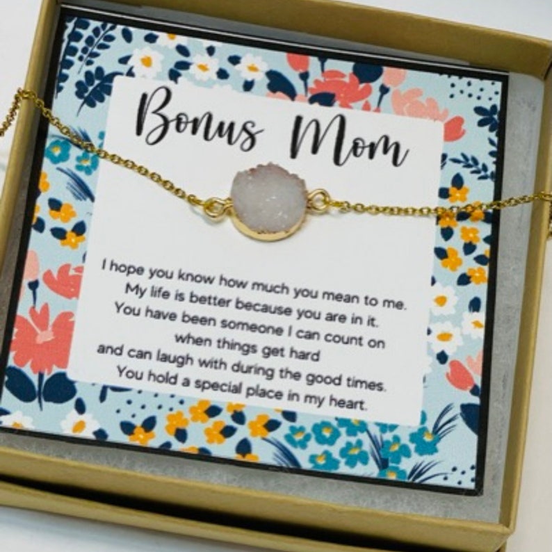 May include: A gold necklace with a white agate stone pendant and a card that reads "Bonus Mom" with a floral pattern. The card says "I hope you know how much you mean to me. My life is better because you are in it. You have been someone I can count on when things get hard and can laugh with during the good times. You hold a special place in my heart."