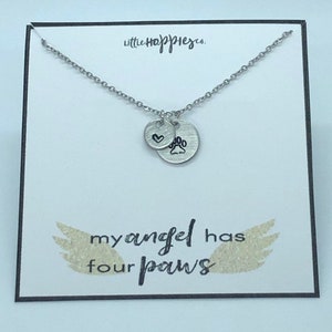 Puede incluir: Collar de plata con un dije de coraz&oacute;n y huella de pata. El collar est&aacute; en una tarjeta blanca con el texto "little happiness" y "my angel has four paws".