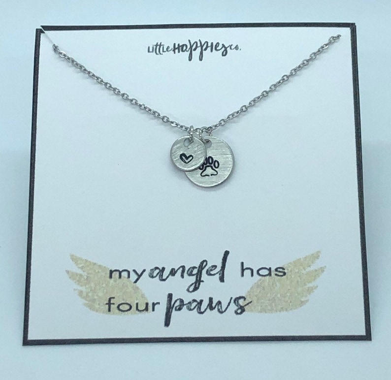 Puede incluir: Collar de plata con un dije de coraz&oacute;n y huella de pata. El collar est&aacute; en una tarjeta blanca con el texto "little happiness" y "my angel has four paws".