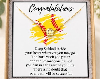May include: A gold-toned chain necklace featuring a small round pendant engraved with a softball heart design. The necklace is displayed on a white card with the text Congratulations and a poem about softball, all inside a square gift box.