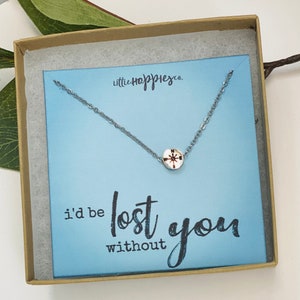 May include: A silver necklace with a compass charm in a light blue box with the text "little happiness co." and "i'd be lost without you".