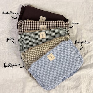 Könnte beinhalten: Eine Sammlung von fünf rechteckigen Reißverschlusstaschen mit gerüschten Rändern und einem kleinen quadratischen Etikett mit der Aufschrift Mi Made Atelier. Die Taschen sind in Dunkelbraun, braunem Karo, grünem Karo, hellgrünem Karo und hellblauem Karo.