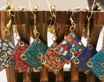 Puede incluir: Seis pares de pendientes cuadrados de mosaico con ganchos dorados. Los pendientes están hechos de pequeños trozos de vidrio en varios colores, incluyendo blanco, rojo, verde, azul y naranja.