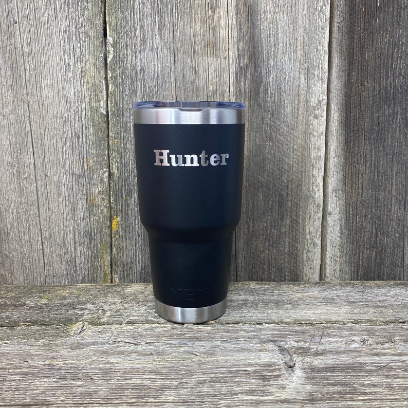 May include: A black stainless steel tumbler with a silver lid and the name "Hunter" engraved on the side.