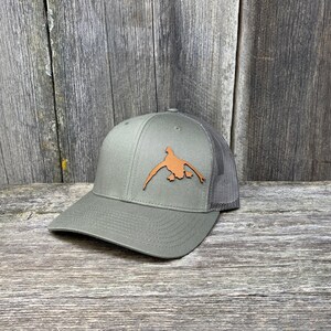 May include: A green and black trucker hat with a brown leather duck silhouette patch on the front.