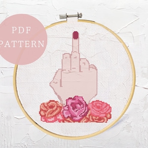 Peut inclure: Modèle de point de croix d'un majeur avec du vernis à ongles rose et trois roses roses. Le motif est dans un cercle de broderie en bois.