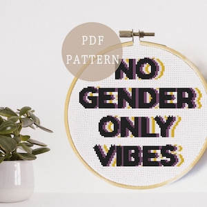 Peut inclure: Un motif de point de croix avec le texte "NO GENDER ONLY VIBES" en lettres noires et violettes avec un contour jaune. Le motif est dans un cercle de broderie en bois.