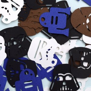 May include: A collection of die-cut paper shapes featuring various character silhouettes in black, white, blue, and brown. The assortment includes helmet designs, droid shapes, and furry creature outlines scattered in a dense, overlapping arrangement.