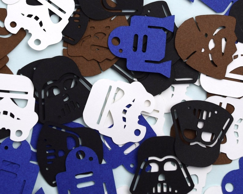 May include: A collection of die-cut paper shapes featuring various character silhouettes in black, white, blue, and brown. The assortment includes helmet designs, droid shapes, and furry creature outlines scattered in a dense, overlapping arrangement.