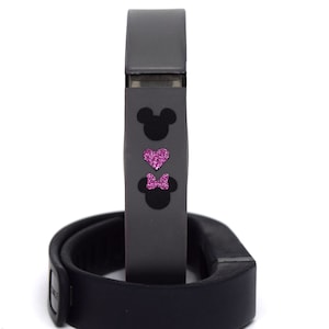 May include: A black fitness tracker with a grey band featuring a pink heart and two black Mickey Mouse silhouettes.