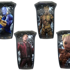 May include: Four different black wristbands with a galaxy background and images of characters from the Marvel Cinematic Universe. The characters are Thanos, Groot, Baby Groot, and Star-Lord.