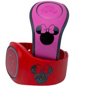 Peut inclure: Deux MagicBands sur le thème de Minnie Mouse. Le bracelet du haut est rose avec une silhouette noire de Minnie Mouse et un nœud rose. Le bracelet du bas est rouge avec une silhouette noire de Minnie Mouse avec un nœud rose pailleté.