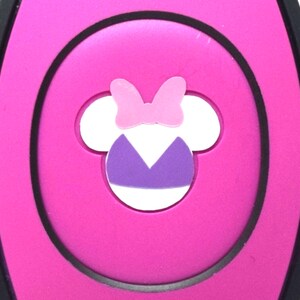 Op de afbeelding: Een roze plastic bedel met een zwarte omtrek. De bedel heeft een wit silhouet van een cartoonmuis die een paarse badpak en een roze strik draagt.