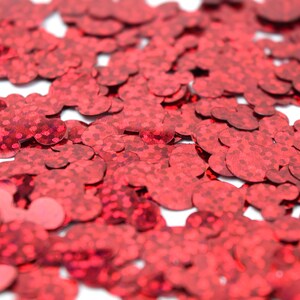 Op de afbeelding: Rode glitterconfetti in de vorm van harten. De confetti is verspreid over een wit oppervlak.