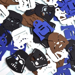 May include: A collection of die-cut paper shapes featuring silhouettes of science fiction characters including black helmets, white stormtrooper masks, blue droids, and brown furry creatures scattered across a flat surface.