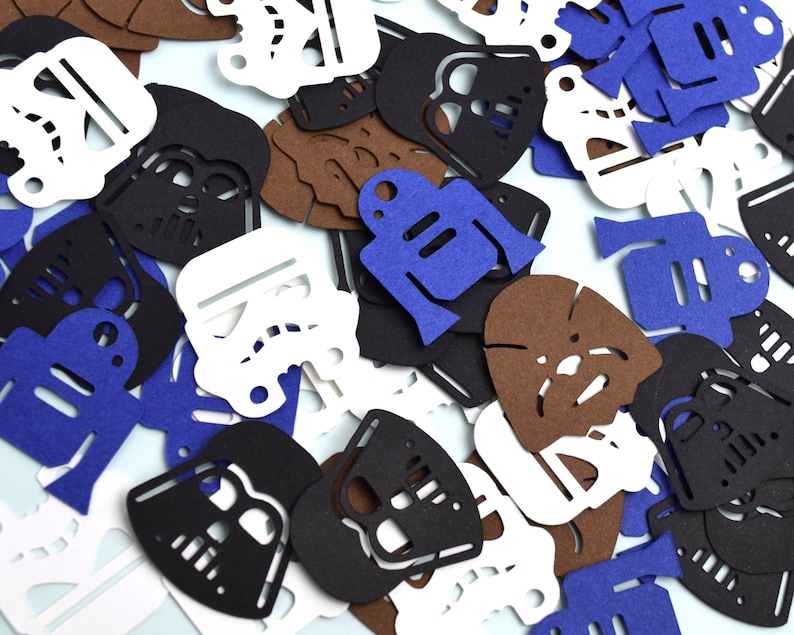 May include: A collection of die-cut paper shapes featuring silhouettes of science fiction characters including black helmets, white stormtrooper masks, blue droids, and brown furry creatures scattered across a flat surface.