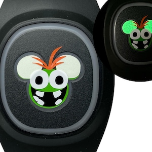 May include: A black silicone wristband with a green and white cartoon character with large eyes and a toothy grin. The character is wearing a red and orange mohawk. The wristband glows in the dark.