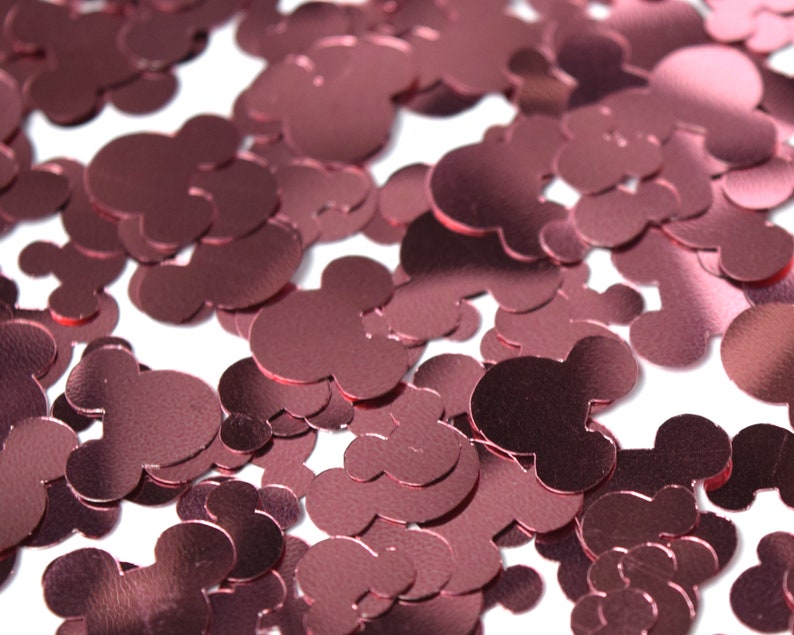 May include: A close-up of rose gold confetti shaped like Mickey Mouse heads. The confetti is scattered on a white background.