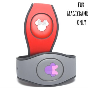 May include: Two MagicBand 2.0 accessories. One is red with a silver glitter Minnie Mouse design, the other is gray with a purple bow design. The text "FOR MAGICBAND 2.0 ONLY" is visible.