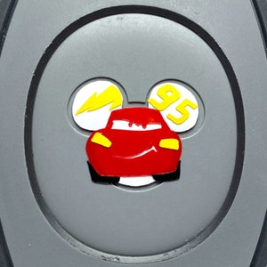 May include: A gray oval-shaped keychain with a red car, a yellow lightning bolt, and the number 95 in yellow on a white background.
