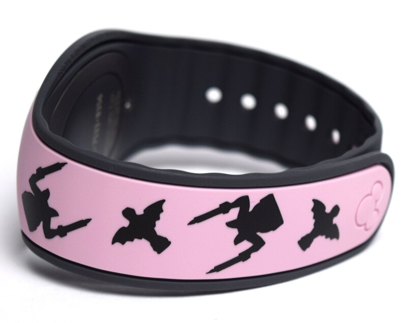 May include: Pink MagicBand with black silhouettes of the Disney villains Maleficent, Ursula, and Cruella de Vil. The band has a black Mickey Mouse icon on the right side.