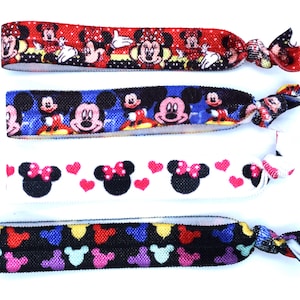 May include: Set of four colorful hair ties featuring a Mickey Mouse and Minnie Mouse design. The hair ties are made of elastic fabric and have a knot at the end.