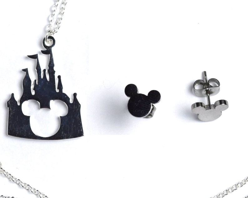 Puede incluir: Un collar de plata con un colgante que presenta una silueta del castillo de Disney con las orejas de Mickey Mouse recortadas. El collar viene con un par de pendientes de plata con forma de orejas de Mickey Mouse.