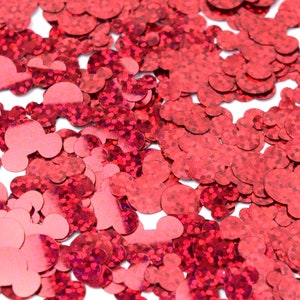 Op de afbeelding: Rode glitterconfetti in de vorm van Mickey Mouse-koppen. De confetti is verspreid over een witte achtergrond.
