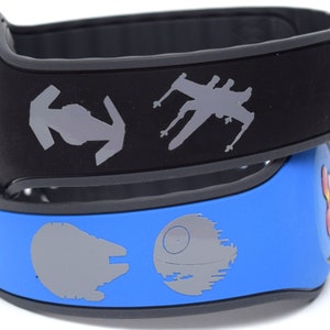 Könnte beinhalten: Zwei schwarze und blaue Silikon-Armbänder mit Star Wars-Motiven. Das obere Armband zeigt einen TIE-Jäger, einen X-Wing und das Symbol der Rebellenallianz. Das untere Armband zeigt einen Todesstern, den Millennium Falcon und einen Mickey-Maus-Kopf.