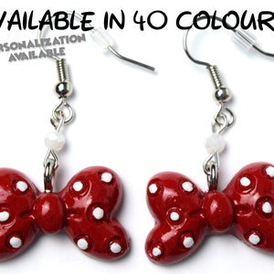 以下が含まれることがあります： 白のドット模様の赤いボウタイのイヤリング。イヤリングはポリマークレイ製で、シルバーのフックが付いています。