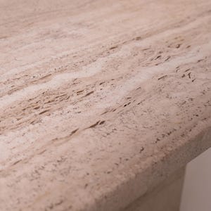 Pu&ograve; includere: Primo piano di una superficie in pietra beige chiaro con un motivo strutturato e poroso. La pietra ha un aspetto naturale e terroso con variazioni di colore e venature. La superficie sembra far parte di una struttura pi&ugrave; grande, forse un tavolo o un piano di lavoro.