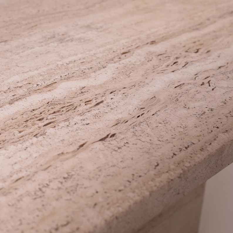 Pu&ograve; includere: Primo piano di una superficie in pietra beige chiaro con un motivo strutturato e poroso. La pietra ha un aspetto naturale e terroso con variazioni di colore e venature. La superficie sembra far parte di una struttura pi&ugrave; grande, forse un tavolo o un piano di lavoro.