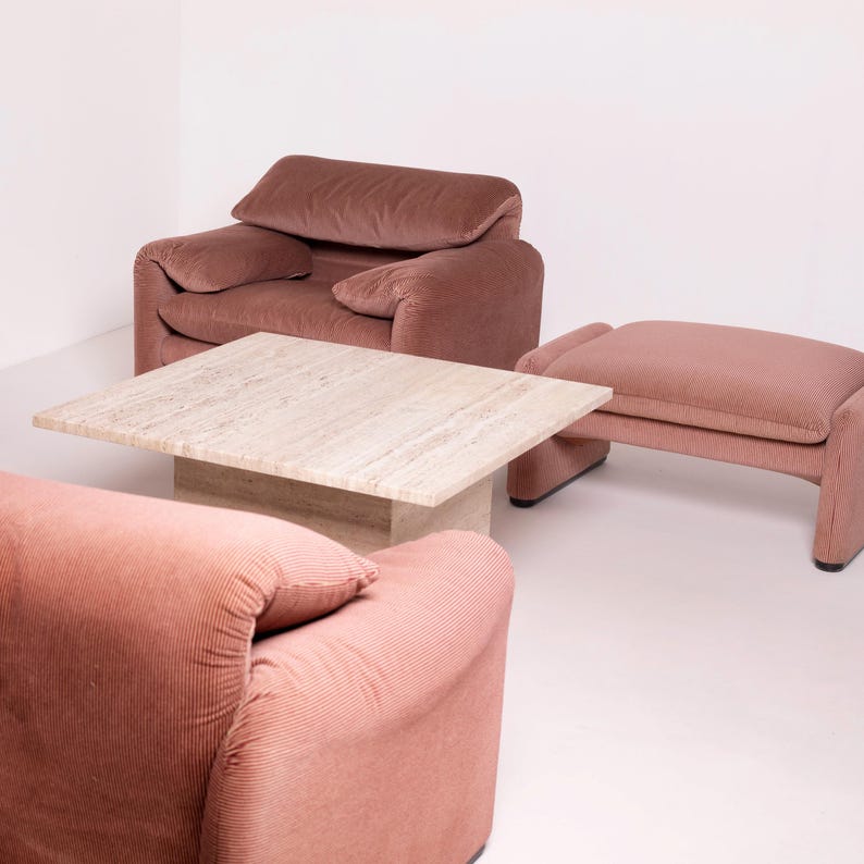 Pu&ograve; includere: Un set da soggiorno con un tavolino quadrato in travertino e due poltrone in velluto a coste color rosa antico. Un pouf nello stesso colore e materiale completa il set. L'arredamento &egrave; ambientato su uno sfondo bianco.