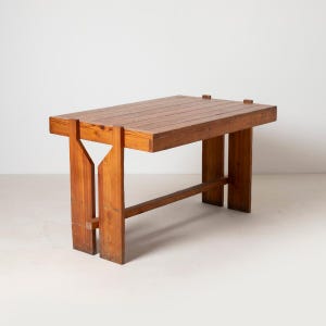 Peut inclure: Une table rectangulaire en bois avec une finition naturelle. La table a un dessus à lattes et est soutenue par des pieds épais et angulaires avec une découpe triangulaire distinctive. La table mesure environ 122 cm de long.