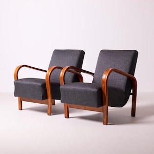 May include: A pair of armchairs featuring dark charcoal grey fabric upholstery and curved wooden armrests. Each chair has a straight backrest, a square seat cushion, and four wooden legs that support the frame structure.