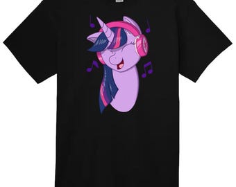 May include: Black t-shirt featuring a cartoon image of a purple unicorn wearing pink headphones and listening to music. The unicorn has a pink horn, blue eyes, and a pink and blue mane.