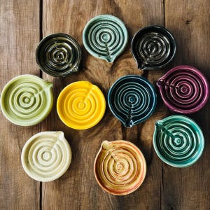 May include: A white ceramic mug with a black handle and the text "But First, Coffee" in a bold, black font. The mug is set against a blurred background, suggesting a cozy setting.