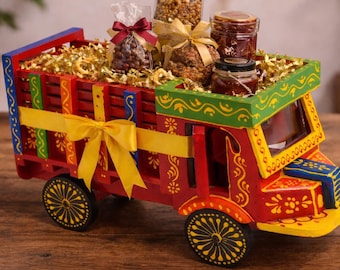 May include: A vibrant, hand-painted wooden truck filled with treats. The red truck features yellow, green, and blue accents, a yellow bow, and black wheels. The bed of the truck is filled with golden filler and small jars.