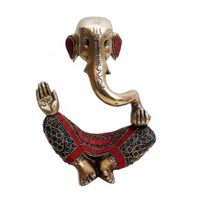 May include: A gold-colored brass statue of Ganesha, the Hindu god of wisdom and prosperity, sitting in a meditative pose. The statue is decorated with red and green gemstones.