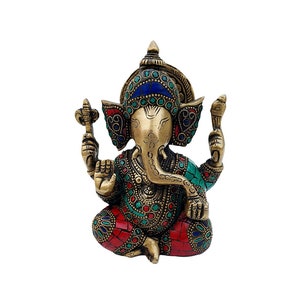 May include: A small, gold-colored statue of Ganesha, the Hindu god of wisdom and prosperity. The statue is decorated with colorful gemstones and has a red and green patterned base.