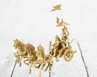 May include: A gold-colored metal sculpture of a chariot pulled by three horses. The chariot is decorated with intricate details and features a figure of a man sitting on a throne. The sculpture is set against a white background.