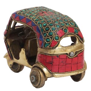 May include: A small, gold-colored metal model of an auto rickshaw, or tuk-tuk, decorated with red, green, and blue mosaic tiles.