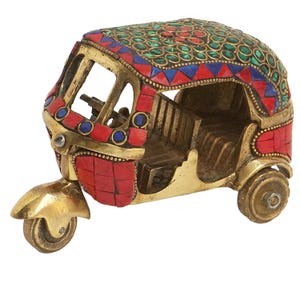 May include: A small, gold-colored metal model of an auto rickshaw, also known as a tuk-tuk, decorated with red, blue, and green mosaic tiles.