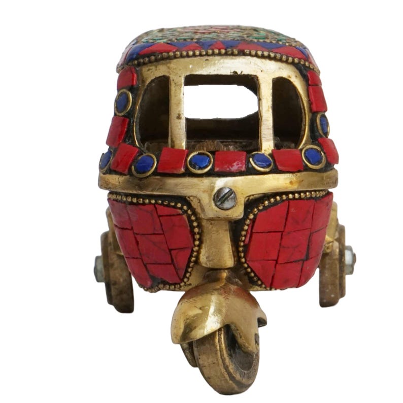 May include: A small, decorative brass auto rickshaw with red and blue mosaic tile accents. The rickshaw has a detailed design and is a traditional Indian souvenir.